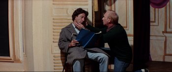 Movie still from “Tootsie” (1982), directed by Sydney Pollack – A man sitting next to another man while holding a book; Medium shot, Over the shoulder angle