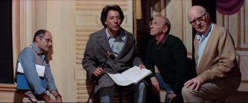 Movie still from “Tootsie” (1982), directed by Sydney Pollack – A man sitting next to another man while holding a book; Medium shot, Low angle