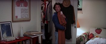 Movie still from “Tootsie” (1982), directed by Sydney Pollack – A man holding a cell phone while standing next to a closet; Medium shot, Over the shoulder angle