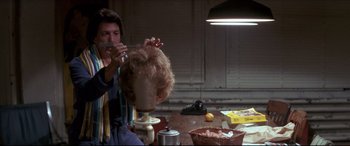 Movie still from “Tootsie” (1982), directed by Sydney Pollack – A man sitting in front of a table cutting a wig; Medium shot, Over the shoulder angle