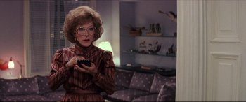 Movie still from “Tootsie” (1982), directed by Sydney Pollack – An older woman holding a cell phone while standing in a living room; Medium shot, Over the shoulder angle
