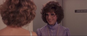 Movie still from “Tootsie” (1982), directed by Sydney Pollack – A woman in a purple shirt and pearls looking at her reflection in a mirror; Close Up shot, Over the shoulder angle
