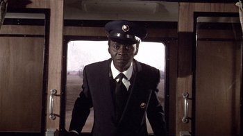 Movie still from “Top Secret!” (1984), directed by Jim Abrahams – A man in a suit and hat standing in a train car; Medium shot, Low angle