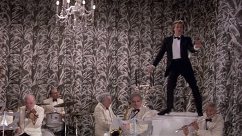 Movie still from “Top Secret!” (1984), directed by Jim Abrahams – A man in a tuxedo standing on top of a stage; Wide shot, Overhead angle
