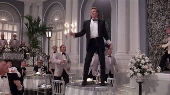 Movie still from “Top Secret!” (1984), directed by Jim Abrahams – A group of men in tuxedos standing around a table; Wide shot, Low angle