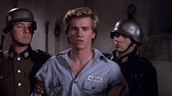 Movie still from “Top Secret!” (1984), directed by Jim Abrahams – A man with a number on his shirt is standing next to another man; Close Up shot, Over the shoulder angle