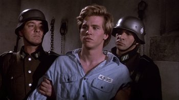 Movie still from “Top Secret!” (1984), directed by Jim Abrahams – A man in a blue shirt is in front of two other men; Medium shot, Over the shoulder angle