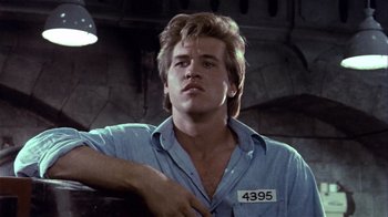 Movie still from “Top Secret!” (1984), directed by Jim Abrahams – A man in a blue button up shirt with a number on his chest; Close Up shot, Low angle