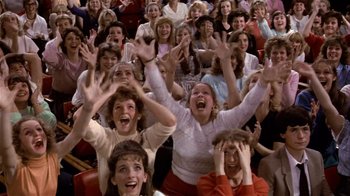 Movie still from “Top Secret!” (1984), directed by Jim Abrahams – A group of people sitting in front of each other with their hands in the air; Wide shot, High angle