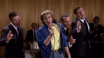 Movie still from “Top Secret!” (1984), directed by Jim Abrahams – A group of men standing next to each other holding microphones; Medium shot, Low angle