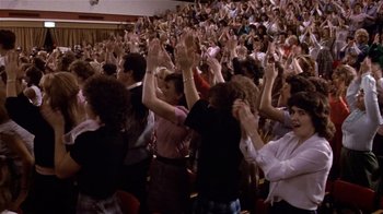 Movie still from “Top Secret!” (1984), directed by Jim Abrahams – A crowd of people in a room with their hands up; Wide shot, High angle