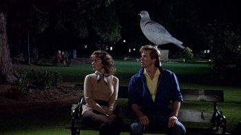Movie still from “Top Secret!” (1984), directed by Jim Abrahams – A man and a woman sitting on a bench with a bird perched on top of their head; Wide shot, Low angle