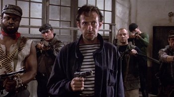 Movie still from “Top Secret!” (1984), directed by Jim Abrahams – A man holding a gun while standing in front of other men; Medium shot, Low angle
