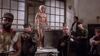 Movie still from “Top Secret!” (1984), directed by Jim Abrahams – A shirtless man in a room with other men; Wide shot, Low angle