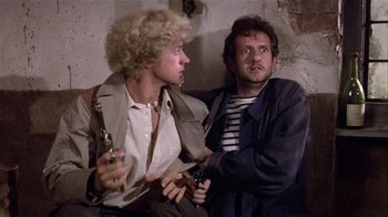 Movie still from “Top Secret!” (1984), directed by Jim Abrahams – A couple of men sitting next to each other holding guns; Medium shot, Low angle