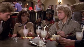 Movie still from “Top Secret!” (1984), directed by Jim Abrahams – A group of people sitting at a table with drinks in front of them; Medium shot, Over the shoulder angle