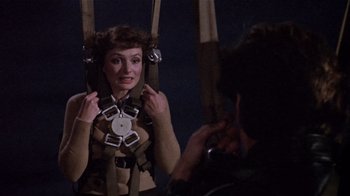 Movie still from “Top Secret!” (1984), directed by Jim Abrahams – A woman is hanging in a sling by a camera; Medium shot, Over the shoulder angle