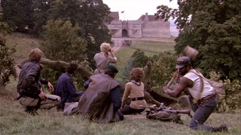 Movie still from “Top Secret!” (1984), directed by Jim Abrahams – A group of people sitting on the ground in a field; Wide shot, High angle