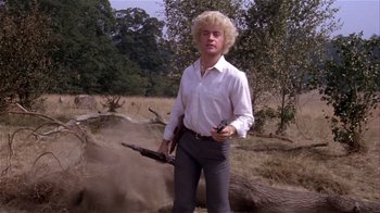 A man in a white shirt holding a gun in a field