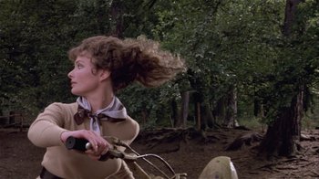 Movie still from “Top Secret!” (1984), directed by Jim Abrahams – A woman riding a bicycle in a wooded area; Close Up shot, Low angle