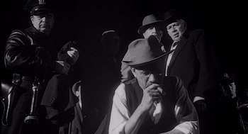 Movie still from “Touch of Evil” (1958), directed by Orson Welles – A black and white photo of a group of men smoking; Medium shot, Low angle