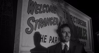 Movie still from “Touch of Evil” (1958), directed by Orson Welles – A black and white photo of a man in front of a sign; Medium shot, Low angle