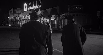 Movie still from “Touch of Evil” (1958), directed by Orson Welles – A black and white photo of a group of men walking down a street; Medium shot, Over the shoulder angle