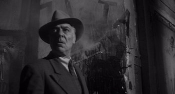 Movie still from “Touch of Evil” (1958), directed by Orson Welles – A man in a suit and a hat standing in front of a building; Medium shot, Low angle