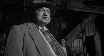 Movie still from “Touch of Evil” (1958), directed by Orson Welles – A black and white photo of a man in a suit and tie; Medium shot, Low angle