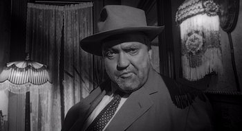 Movie still from “Touch of Evil” (1958), directed by Orson Welles – A man wearing a suit and a hat in a black and white photo; Close Up shot, Low angle