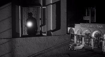 Movie still from “Touch of Evil” (1958), directed by Orson Welles – A man standing on a window ledge looking out of a window at night; Wide shot, Low angle