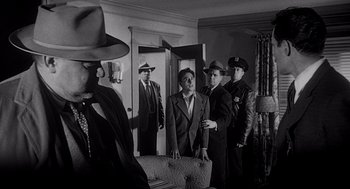 Movie still from “Touch of Evil” (1958), directed by Orson Welles – A black and white photo of a group of men standing in a room; Medium shot, Over the shoulder angle