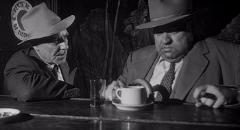 Movie still from “Touch of Evil” (1958), directed by Orson Welles – Two men sitting at a table drinking coffee; Medium shot, High angle