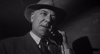 Movie still from “Touch of Evil” (1958), directed by Orson Welles – An older man wearing a suit and a hat talking on a phone; Close Up shot, Low angle