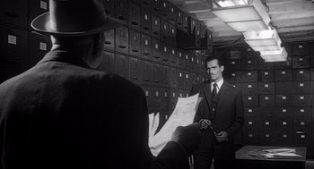 Movie still from “Touch of Evil” (1958), directed by Orson Welles – A man in a suit and tie holding a paper; Medium shot, Low angle