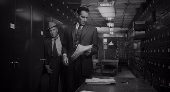 Movie still from “Touch of Evil” (1958), directed by Orson Welles – Two men in suits and hats are looking at papers; Medium shot, Low angle