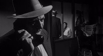 Movie still from “Touch of Evil” (1958), directed by Orson Welles – A man talking on a phone in front of two other men; Medium shot, Over the shoulder angle