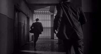 Movie still from “Touch of Evil” (1958), directed by Orson Welles – A man in a suit and tie walking down a hall way; Wide shot, Low angle