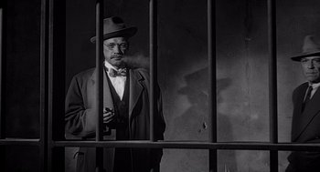 Movie still from “Touch of Evil” (1958), directed by Orson Welles – An old man smoking a cigarette in front of a jail cell; Medium shot, Low angle