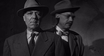 Movie still from “Touch of Evil” (1958), directed by Orson Welles – A man in a suit and a man in a hat; Close Up shot, Low angle