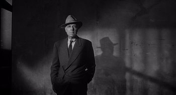 Movie still from “Touch of Evil” (1958), directed by Orson Welles – An older man wearing a suit and hat in front of a concrete wall; Medium shot, Low angle