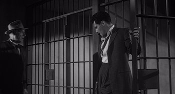Movie still from “Touch of Evil” (1958), directed by Orson Welles – A black and white photo of a man standing in front of bars; Medium shot, Low angle