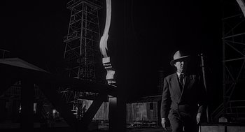 Movie still from “Touch of Evil” (1958), directed by Orson Welles – A man in a suit and hat standing next to a pole; Wide shot, Low angle