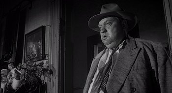 Movie still from “Touch of Evil” (1958), directed by Orson Welles – An older man wearing a hat and a tie; Medium shot, Low angle