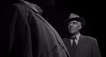 Movie still from “Touch of Evil” (1958), directed by Orson Welles – A man wearing a suit and a hat standing next to another man wearing a suit; Medium shot, Low angle