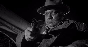 Movie still from “Touch of Evil” (1958), directed by Orson Welles – A man holding a gun in a black and white photo; Close Up shot, Low angle