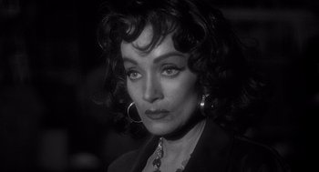 Movie still from “Touch of Evil” (1958), directed by Orson Welles – Black and white photograph of a woman in a black suit; Close Up shot, Over the shoulder angle