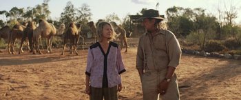 Movie still from “Tracks” (2013), directed by John Curran – A man and a woman standing next to each other in front of a herd of camels; Medium shot, Over the shoulder angle