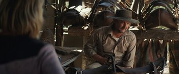 Movie still from “Tracks” (2013), directed by John Curran – A man sitting in front of a table with a hat on it; Medium shot, Over the shoulder angle
