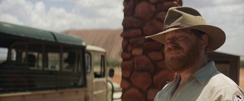 Movie still from “Tracks” (2013), directed by John Curran – A man with a beard wearing a hat standing in front of a truck; Medium shot, Over the shoulder angle